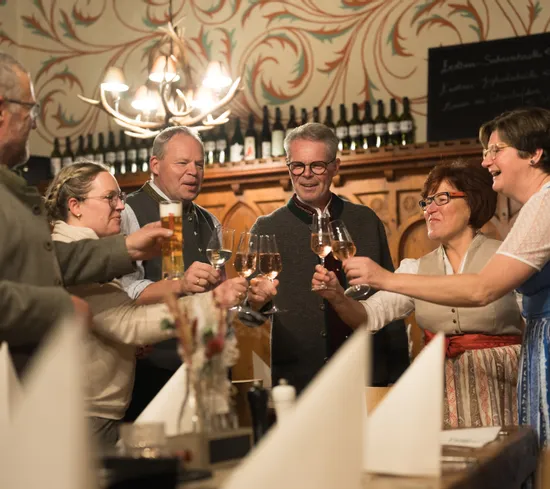 Gruppo di persone in abiti tradizionali brinda con vino e birra in un ristorante accogliente
